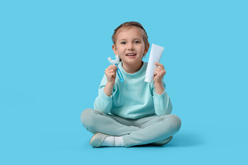 Happy little girl with brush and toothpaste sitting on blue background