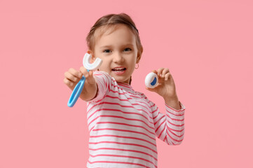 Happy little girl with toothbrush and dental floss on pink background
