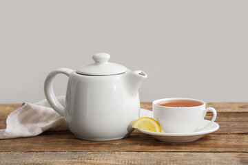 Cup of hot tea, teapot and fabric napkin on wooden table near beige wall