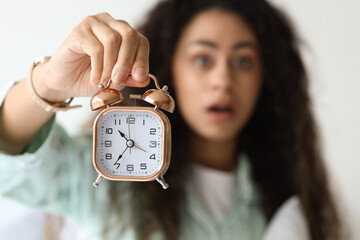 Overslept young African-American woman with alarm clock in bedroom, closeup