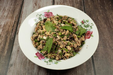 Spicy roasted catfish meat dressing with mint, herbal vegetable and chilly serving on the plate. Famous local fish salad many in Thailand.