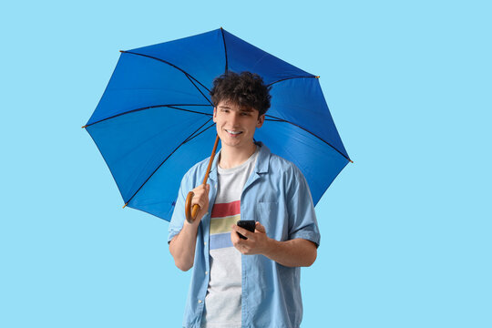 Young man with umbrella and mobile phone on blue background