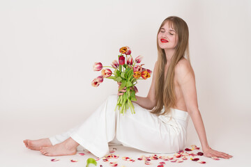 Half naked woman holding bouquet of spring tulips flowers for Woman's Day with closed eyes. Serene blonde woman with long hair falling down and covering her chest. Model sitting on white background
