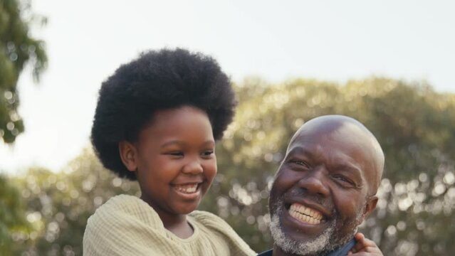 Close up of smiling loving grandfather cuddling laughing granddaughter outdoors in countryside enjoying nature- shot in slow motion