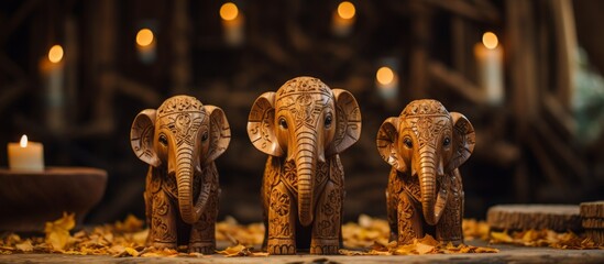 Three intricately carved wooden elephant figurines are placed in a row, with a burning candle illuminating them from behind
