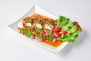 Sliced beef shank salad, spicy and sour flavor, decorated with sliced chili, garlic, salad leaves and tomato. Thai fusion food. Sliced beef shank salad in a white plate isolated on a white background.