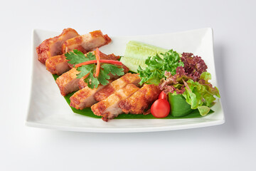 Crispy Fried Pork Belly Slices with Fish Sauce served with salad leaves, tomatoes and cucumber in white plate isolated on white background. Foods that are high in fat.