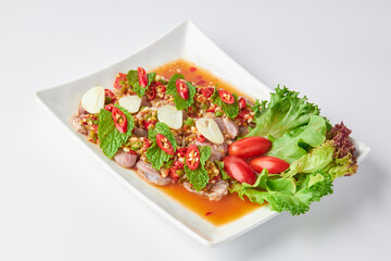 Sliced beef shank salad, spicy and sour flavor, decorated with sliced chili, garlic, salad leaves and tomato. Thai fusion food. Sliced beef shank salad in a white plate isolated on a white background.