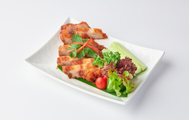 Crispy Fried Pork Belly Slices with Fish Sauce served with salad leaves, tomatoes and cucumber in white plate isolated on white background. Foods that are high in fat.