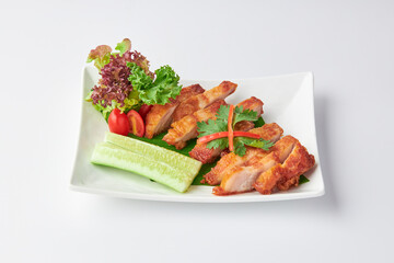 Crispy Fried Pork Belly Slices with Fish Sauce served with salad leaves, tomatoes and cucumber in white plate isolated on white background. Foods that are high in fat.