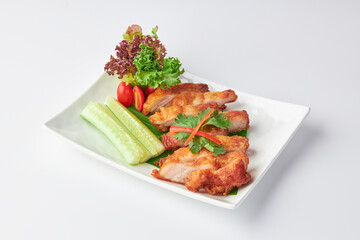 Crispy Fried Pork Belly Slices with Fish Sauce served with salad leaves, tomatoes and cucumber in white plate isolated on white background. Foods that are high in fat.