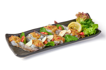 Fresh shrimp soaked in fish sauce and topped with seafood dipping sauce and sliced chili, garlic and mint, garnished with sliced lemon and salad leaves on black plate isolated on white background.