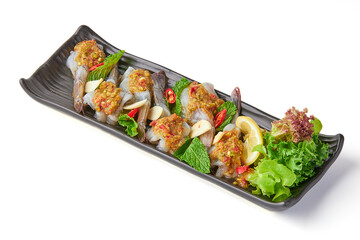 Fresh shrimp soaked in fish sauce and topped with seafood dipping sauce and sliced chili, garlic and mint, garnished with sliced lemon and salad leaves on black plate isolated on white background.