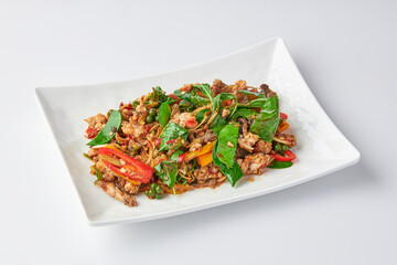Stir fried spicy Frog leg with vegetables and herbs (chilli, galangal, kaffir lime leaves and basil) served on white plate isolated on white background.
