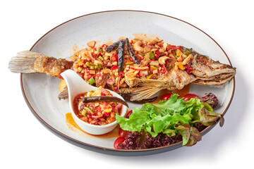 Deep fried fish with Thai spicy mixed herbs salad served with dipping sauce (sliced chili, lime, cashew nut, ginger, shallot) and fresh organic salad on plate isolated in white background