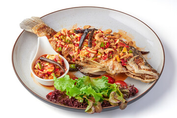 Deep fried fish with Thai spicy mixed herbs salad served with dipping sauce (sliced chili, lime, cashew nut, ginger, shallot) and fresh organic salad on plate isolated in white background