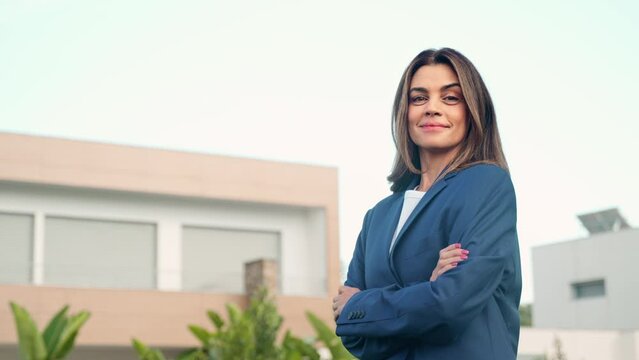 Happy saleswoman realtor or new property buyer modern villa owner standing outside villa or country house. Confident mature older Latin business woman real estate agent outdoors. Portrait.