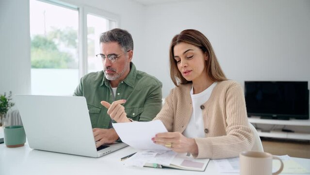 Happy middle aged mature man and woman paying bills online at home. Older senior couple using laptop computer checking insurance or financial invoice counting taxes sitting at table in living room.
