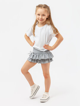 Sports dancing, children's aerobics. A 5-year-old girl stands smiling in a white T-shirt , sneakers and a gray skirt on a white background. Hands on the waist. Photo. Copy space.
