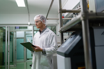 A man in a white lab coat is holding a clipboard and looking at something