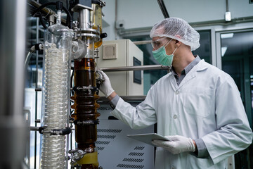 A scientist wearing a lab coat and goggles is writing on a clipboard. The clipboard is black and the scientist is looking at it intently