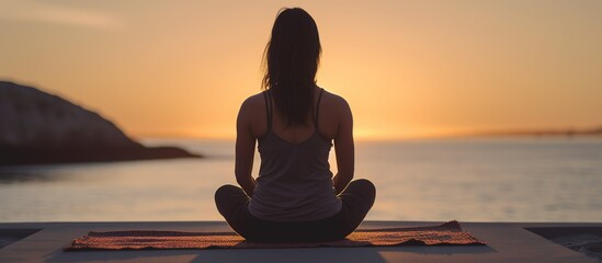seen from behind Beautiful young woman doing yoga exercises on the beach at sunset
