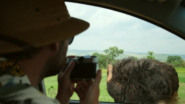 man traveler in safari hat takes photo from vehicle for ostriches. Traveling photographer taking photos during safari. man traveler and photographer standing in desert looking at wildlife animals