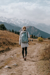 A blond girl hiking in the mountains, snowy peaks in the background, view from the back