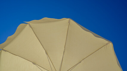 Fototapeta na wymiar White beach umbrella. Blue sky in the background. View from below. Relaxing context. Summer holidays by the sea. General contest and location