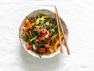 Warm asian style salad with beef and vegetables on a light background, top view