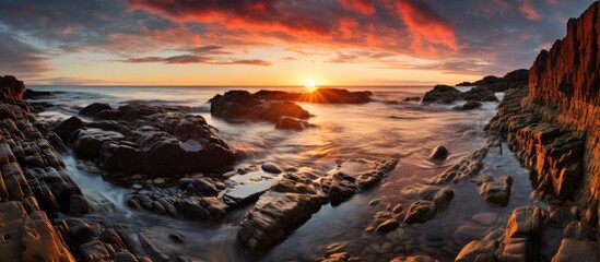 Sunset casting a warm glow over the tranquil ocean, enhancing the beauty of the jagged rocks and...