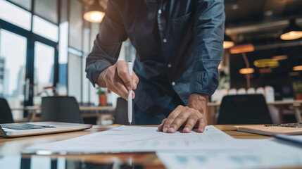 Focused professional examining and pointing to business reports on a wooden desk in a modern office setting..