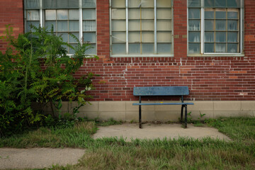 Lonely bench in front of an old school building with overgrown grass.