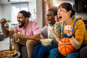 Multiracial group of friends watching basketball game, eating pizza, drinking beer and cheering.