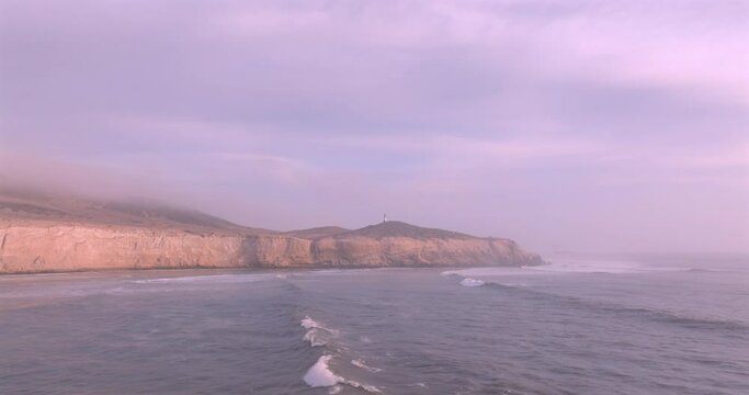 Sea waves, cliffs and lighthouse at sunset with foam near the shore. Sea surface aerial view of sea. Puerto Eten, Peru.
