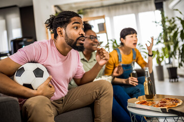Multiracial group of friends watching soccer game, cheering , eating pizza and drinking beer.