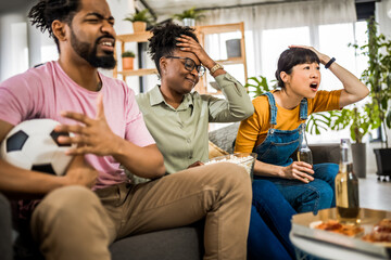 Multiracial group of friends watching soccer game, cheering and drinking beer. Angry because their...
