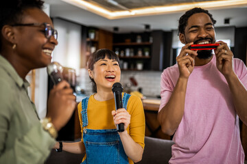 Multiracial group of friends having karaoke night. Singing in to the microphone, drinking beer and playing mouth organ. - obrazy, fototapety, plakaty