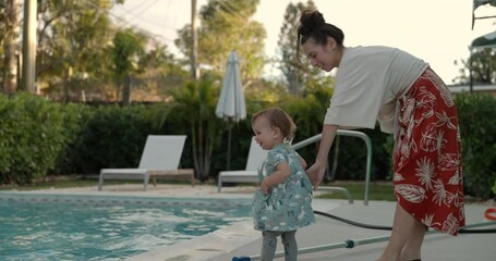 Mother holds back toddler girl as she plays near swimming pool - pool safety