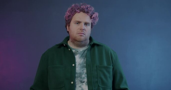 Slow motion portrait of unhappy young man sighing expressing sadness and looking at camera on purple background. Negative emotion and people concept.