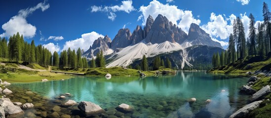 Tranquil alpine lake encircled by jagged rocks and lush green trees in the foreground with a serene mountain backdrop