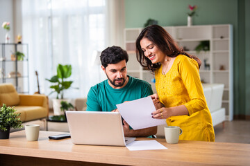 Young Indian couple checking mortgage or loan agreement, financial documents together, using laptop...