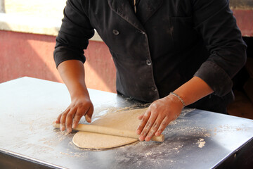 Hands of pizza maker man kneads dough, prepares and shapes for pizza base with rolling pin and flour