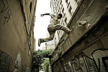 In a deserted alley, parkour practitioners leap and vault, their movements fluid and agile against urban obstacles.