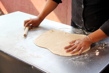 Hands of pizza maker man kneads dough, prepares and shapes for pizza base with rolling pin and flour