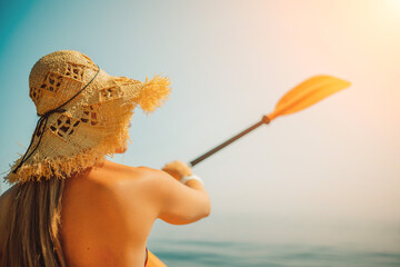 A woman wearing a straw hat is paddling a canoe on a sunny day. Scene is relaxed and carefree, as...