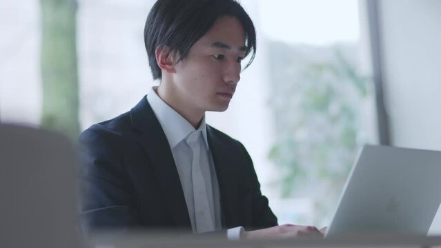 オフィスでパソコンを使って仕事をするスーツを着た若い日本人ビジネスマン	