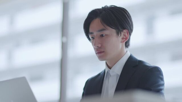 オフィスでパソコンを使って仕事をするスーツを着た若い日本人ビジネスマン	