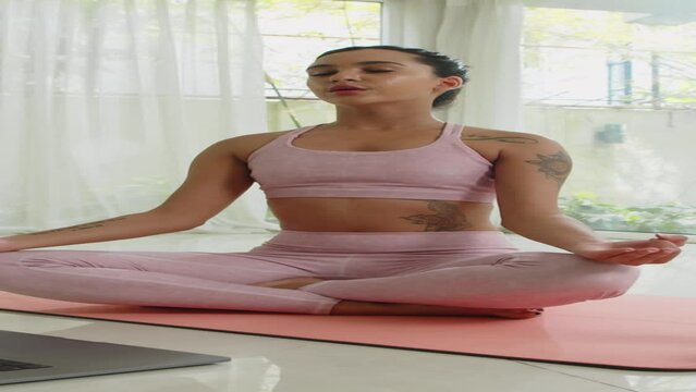 Vertical shot of young female athlete using laptop while training online from home on yoga mat