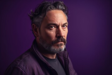 A man with a beard and gray hair is wearing a purple jacket